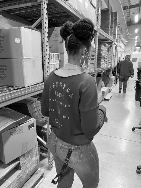 A worker walking the packaging racks in a Natural State Medicinals sweatshirt